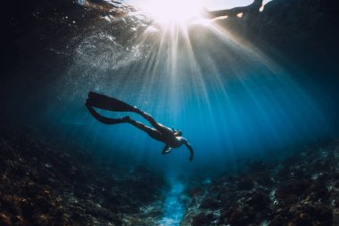 Young freediver woman with fins glides and amazing sun rays. Freediving underwater in sea clipart