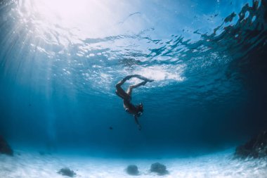 Bikinili serbest kız yüzgeçleri mavi şeffaf okyanusta suyun altında süzülüyor.