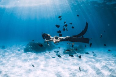Bikinili serbest kız yüzgeçleri mavi şeffaf okyanusta suyun altında süzülüyor.