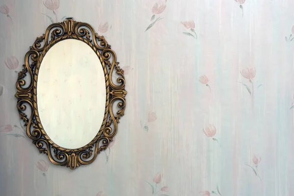 Old antique gold mirror hanging in a vintage room with old pattern wallpaper