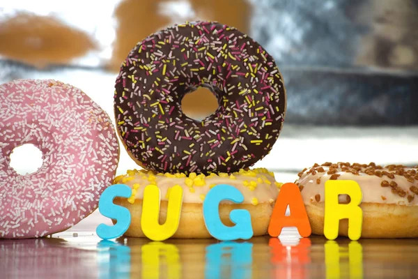 Группа вкусных красочных пончиков с глазурью рядом с красочным фоном со словом сахар — стоковое фото