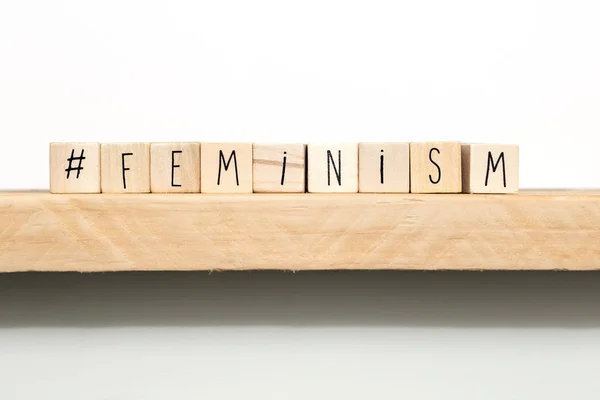 Cubi di legno con un hashtag e la parola femminismo vicino sfondo bianco, concetto di social media — Foto Stock
