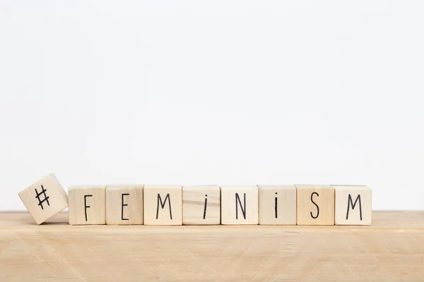 Cubos de madera con un hashtag y la palabra Feminismo cerca de fondo blanco, concepto de redes sociales —  Fotos de Stock
