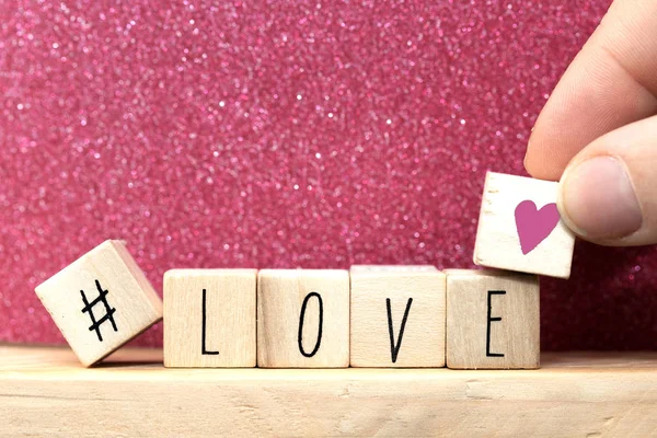 Parola Amore su cubi di legno con cuore rosa e hashtag, primo piano vicino scintillio sfondo rosa — Foto Stock