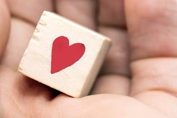 Cubo de madera con un corazón rojo en una mano de personas macro, concepto de San Valentín —  Fotos de Stock