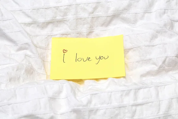Handwritten little yellow note with the words I love you on white sheets on a bed, romantic concept valentines day