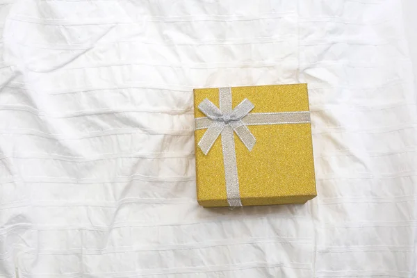 Yellow Gift box. Present box for Holidays on white sheets of a bed Valentines Day gift, International Womens Day gift over white bed linen background. Valentines Gift or birthday closeup