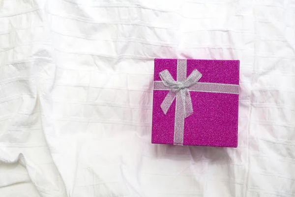 Purple Gift box. Present box for Holidays on white sheets of a bed Valentines Day gift, International Womens Day gift over white bed linen background. Valentines Gift or birthday closeup