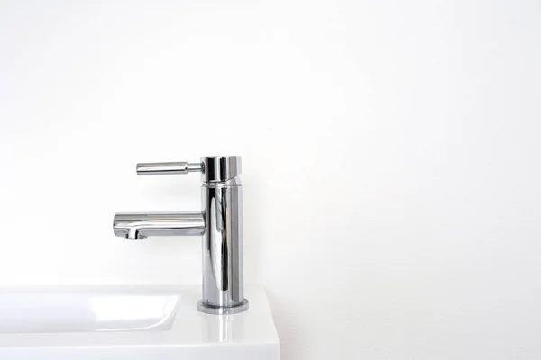 Rubinetto in metallo argento su parete bianca, nuovo lavabo moderno pulito sullo sfondo — Foto Stock
