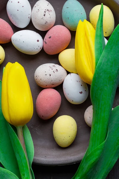 Крашеные красочные пасхальные яйца на старинном деревянном фоне текстуры, мягкие пастели современный дизайн с желтыми тюльпанами — стоковое фото