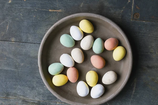 Šedá keramická deska s malovanými velikonočními vejci pastelových barev na vinobraní dřevěné pozadí. Happy Easter card concept, minimalistic design, top view — Stock fotografie
