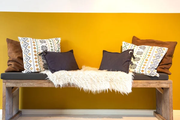 Banco de madera moderno retro con almohadas blancas, marrones y beige cerca de la pared amarilla brillante Interior del hogar moderno. lugar acogedor —  Fotos de Stock