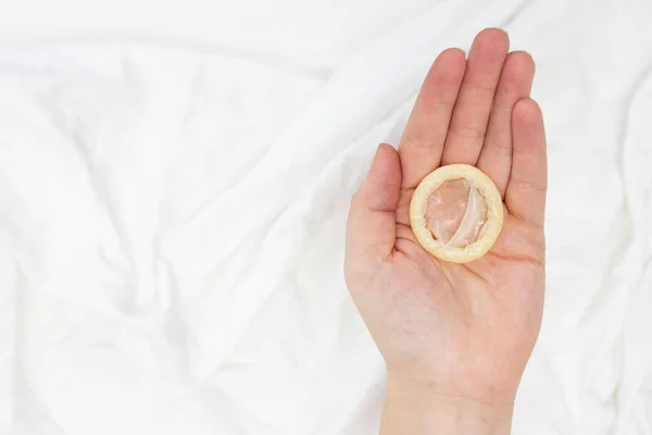 Koncepcja bezpiecznego seksu. Ręczne trzymanie prezerwatywy z białymi prześcieradłami — Zdjęcie stockowe