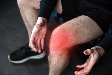 Acı içinde dizine uzanan kaslı bir adamın portresi spor salonunda spor yaparken bacağı kırmızı ile çevrili bir şekilde yaralanan erkekler.