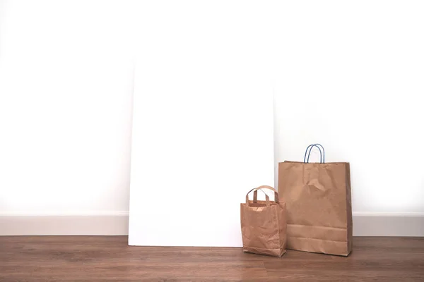 Braune leere Einkaufstaschen mit leerem Plakatrahmen vor weißer Wand, Platz für Text. Einkaufskonzept — Stockfoto