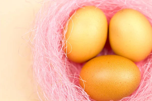 Easter yellow eggs in pastel pink nest on yellow background. Close up in minimalism style.