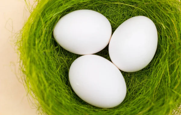 パステル黄色の背景に緑の巣でイースターの白い卵 ミニマリズムのスタイルを閉じる — ストック写真