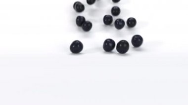 Beyaz yüzeyde bir sürü siyah zeytin yuvarlanıyor. Taze 3 boyutlu gerçekçi sebzelerin düşüşünü ve yuvarlanmasını kapatın. 4k canlandırma görüntüsü.
