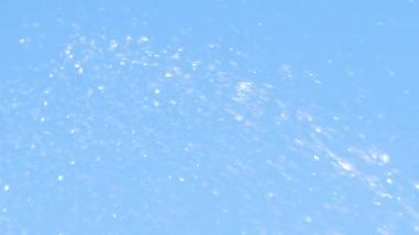 Su damlaları mavi gökyüzü arka planında yavaş çekimde uçuyor. Su sıçratmaya yakın. Soyut arkaplan görüntüleri.