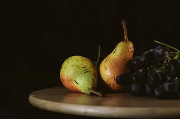 Martwa natura gruszki i czarne winogrona na czarnym tle — Zdjęcie stockowe