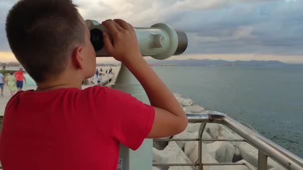 Een jongetje kijkt door een openbare verrekijker — Stockvideo