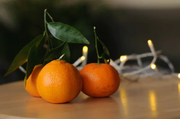 Ein paar saftige und köstliche Mandarinen auf dem Tisch im Licht weißer Girlanden — Stockfoto