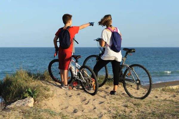 Oğlan ve genç kadın deniz kıyısındaki bir uçurumda bisiklete biniyorlar.