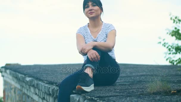 Mladá bruneta dívka sedí na střeše rodinného domu. — Stock video