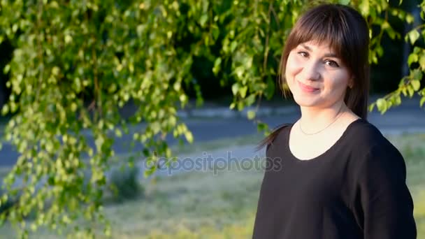 Chica morena en vestido negro y el pelo largo sonríe a la cámara — Vídeos de Stock