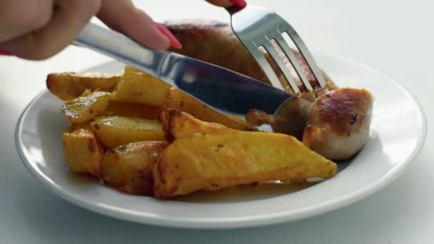 Full HD video footage. A girl is cutting a fried sausage on a white plate. — Stock Video