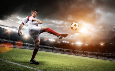 Futbolcu stadyumda bir topa vuruyor.