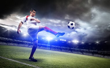 Futbolcu stadyumda bir topa vuruyor.