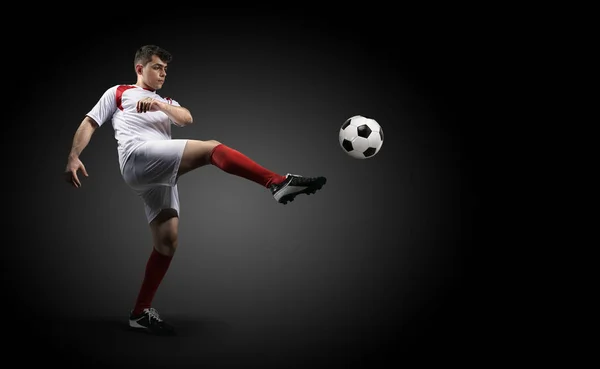 Jugador de fútbol está pateando una pelota en el fondo negro . — Foto de Stock