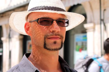 Beyaz şapkalı bir adam sokaklarda yürüyor..