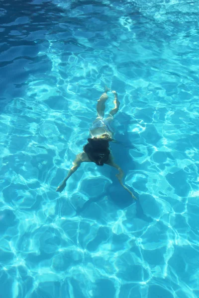 Una giovane ragazza che nuota nell'acqua blu della piscina — Foto Stock