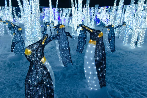 Penguin toy. Christmas decoration and luminous garland, and many glowing light bulbs. — Stock Photo, Image