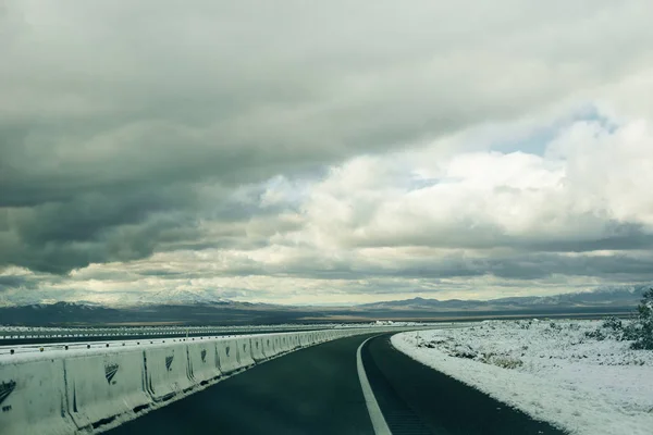 Dobre ao longo de uma estrada coberta de neve em um cenário de montanha no inverno — Fotografia de Stock