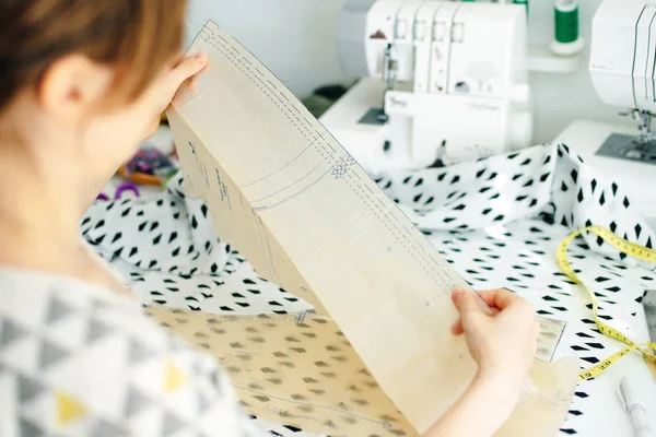 Top view of workplace of seamstress. Dressmaker cuts detail on sketch. Seamstress cuts pink fabric with scissors. — Stock Photo, Image