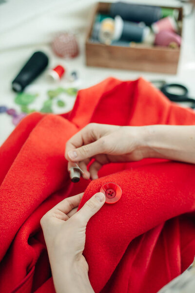 a seamstress sews a button on a red coat on white table
