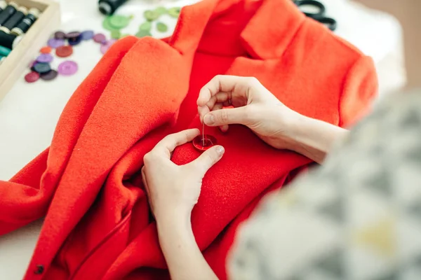 Uma costureira cose um botão em um casaco vermelho na mesa branca — Fotografia de Stock