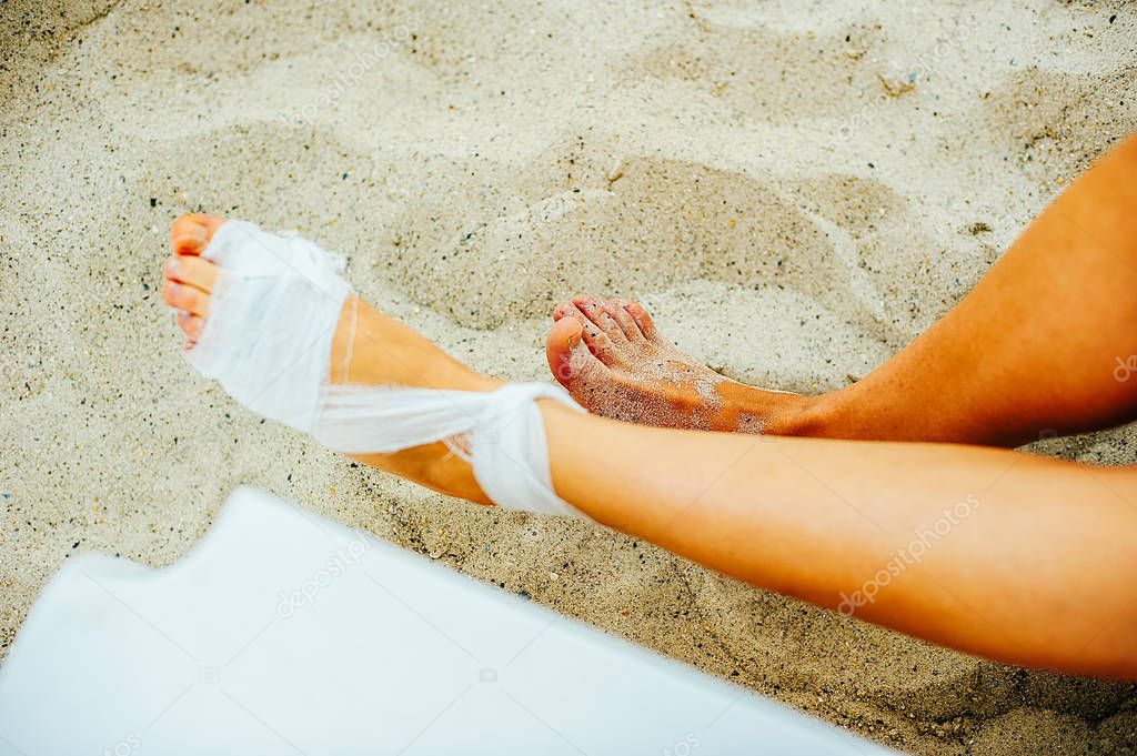 Gauze bandage the treating patients with man is wrapping his foot injury on the beach