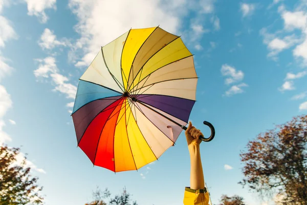 Junge Frau steht mit einem bunten Regenschirm und dreht ihn bei blauem Himmel gegen — Stockfoto