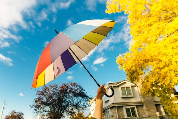 Jovem mulher de pé com um guarda-chuva multi-colorido e gira-lo contra com um céu azul — Fotografia de Stock