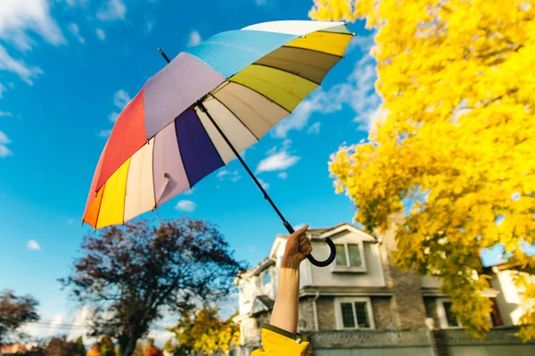 Jovem mulher de pé com um guarda-chuva multi-colorido e gira-lo contra com um céu azul — Fotografia de Stock