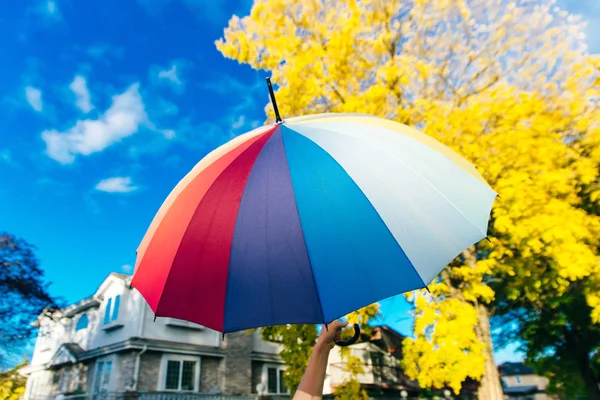 Jovem mulher de pé com um guarda-chuva multi-colorido e gira-lo contra com um céu azul — Fotografia de Stock