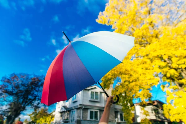 Jovem mulher de pé com um guarda-chuva multi-colorido e gira-lo contra com um céu azul — Fotografia de Stock