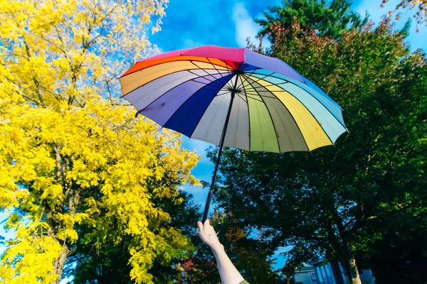 Jovem mulher de pé com um guarda-chuva multi-colorido e gira-lo contra com um céu azul — Fotografia de Stock