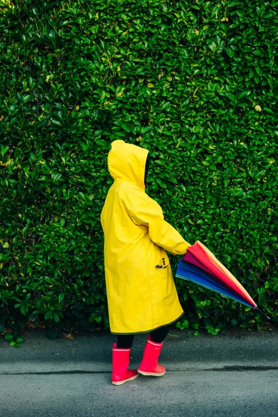 Menina em uma capa de chuva amarela em um fundo de uma parede com grama — Fotografia de Stock