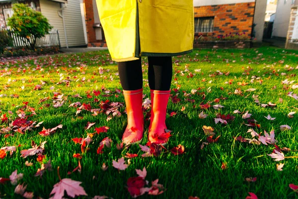 yellow raincoat. Rubber pink boots against. Conceptual image of legs in boots on green grass.