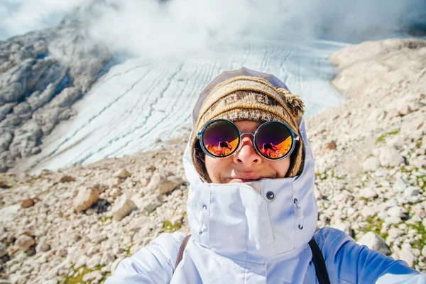 Menina turística em óculos de sol faz selfie em um fundo de montanhas — Fotografia de Stock